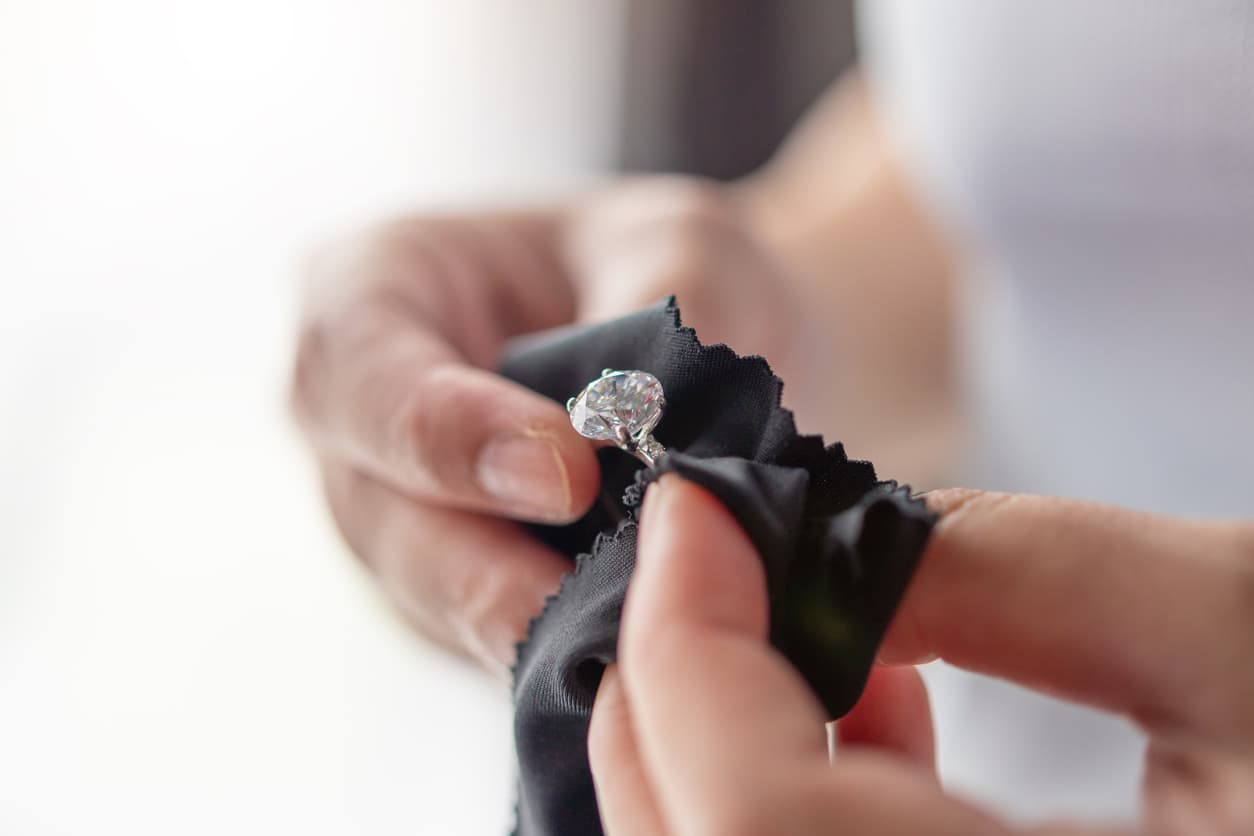 Closeup photo of womans hands cleaning a Moissanite diamond with cloth